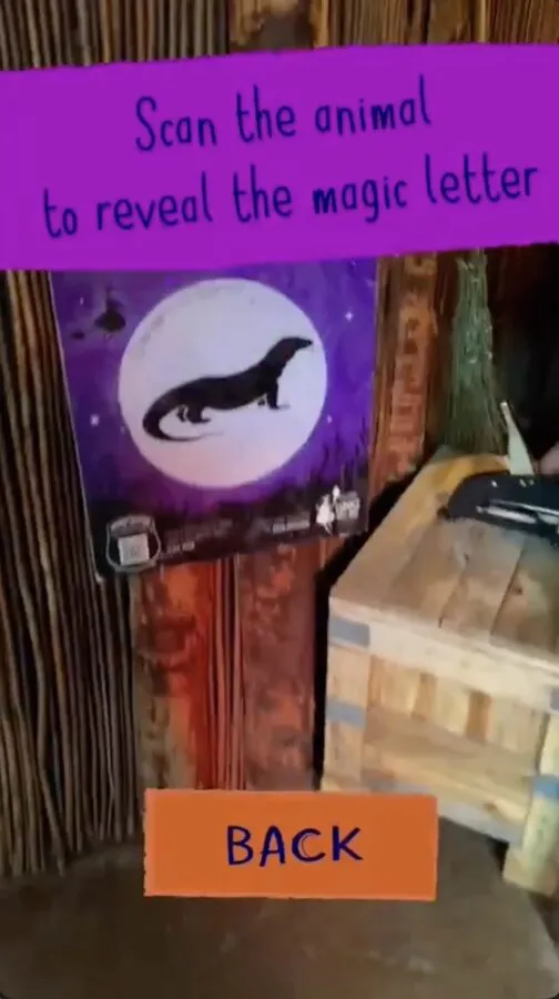 A phone browser showing the prompt "Scan the animal to reveal the magic letter" pointed at a purple panel with an animal silhouette at a trail station
