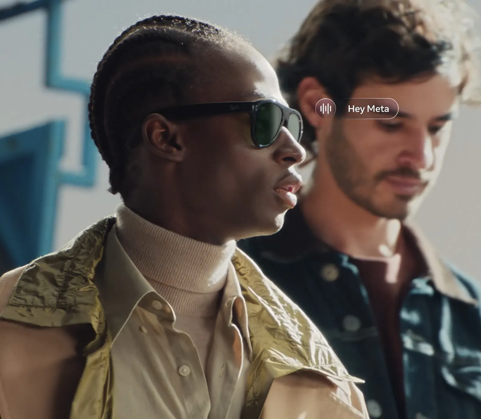 Two people, one wearing Ray-Ban Meta sunglasses, with a Hey Meta voice prompt shown beside the frames